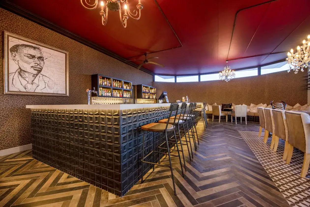 Etosha King Nehale Rates 2026 & Booking — Lodge at King Nehale Gate, Northern Etosha 4 Cocktail bar at Etosha King Nehale with a portrait of King Nehale, chandeliers and herringbone flooring