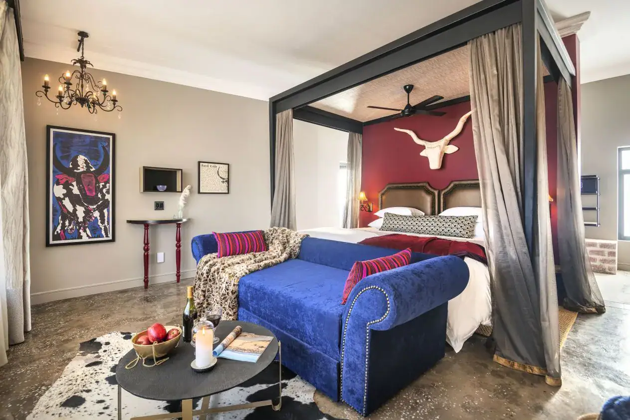 Etosha King Nehale Rates 2026 & Booking — Lodge at King Nehale Gate, Northern Etosha 2 Four-poster bedroom suite at Etosha King Nehale with royal-blue daybed and Oshiwambo cattle-horn wall art