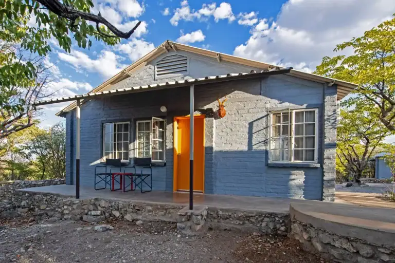 Blue-painted chalet with orange door at Etosha Safari Camp