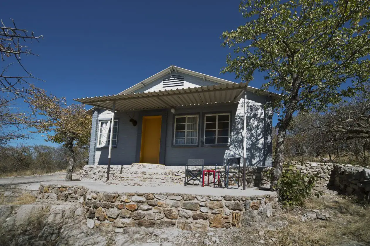 Blue-grey brick chalet with yellow front door and stone-walled terrace at Etosha Safari Camp