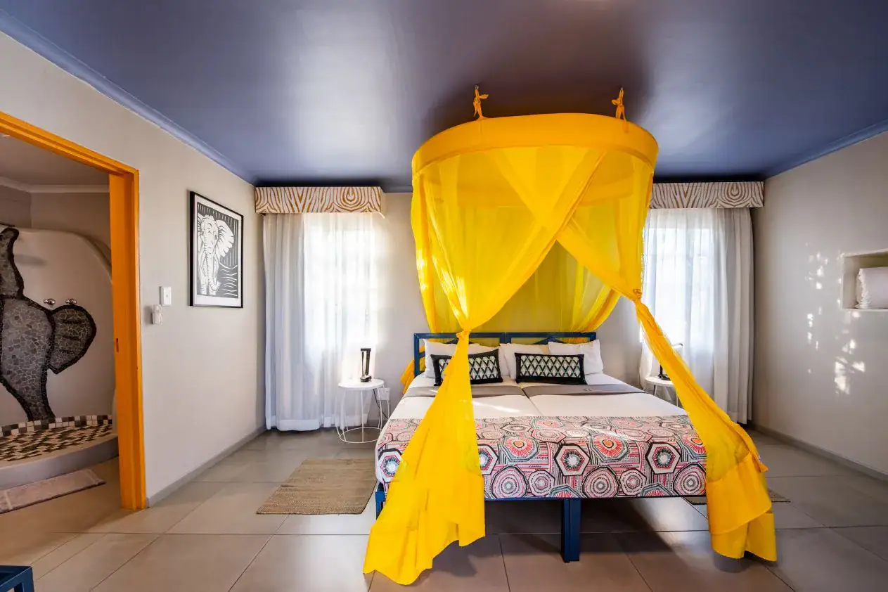 Double room at Etosha Safari Camp with a round yellow canopy net, blue ceiling and elephant linocut artwork