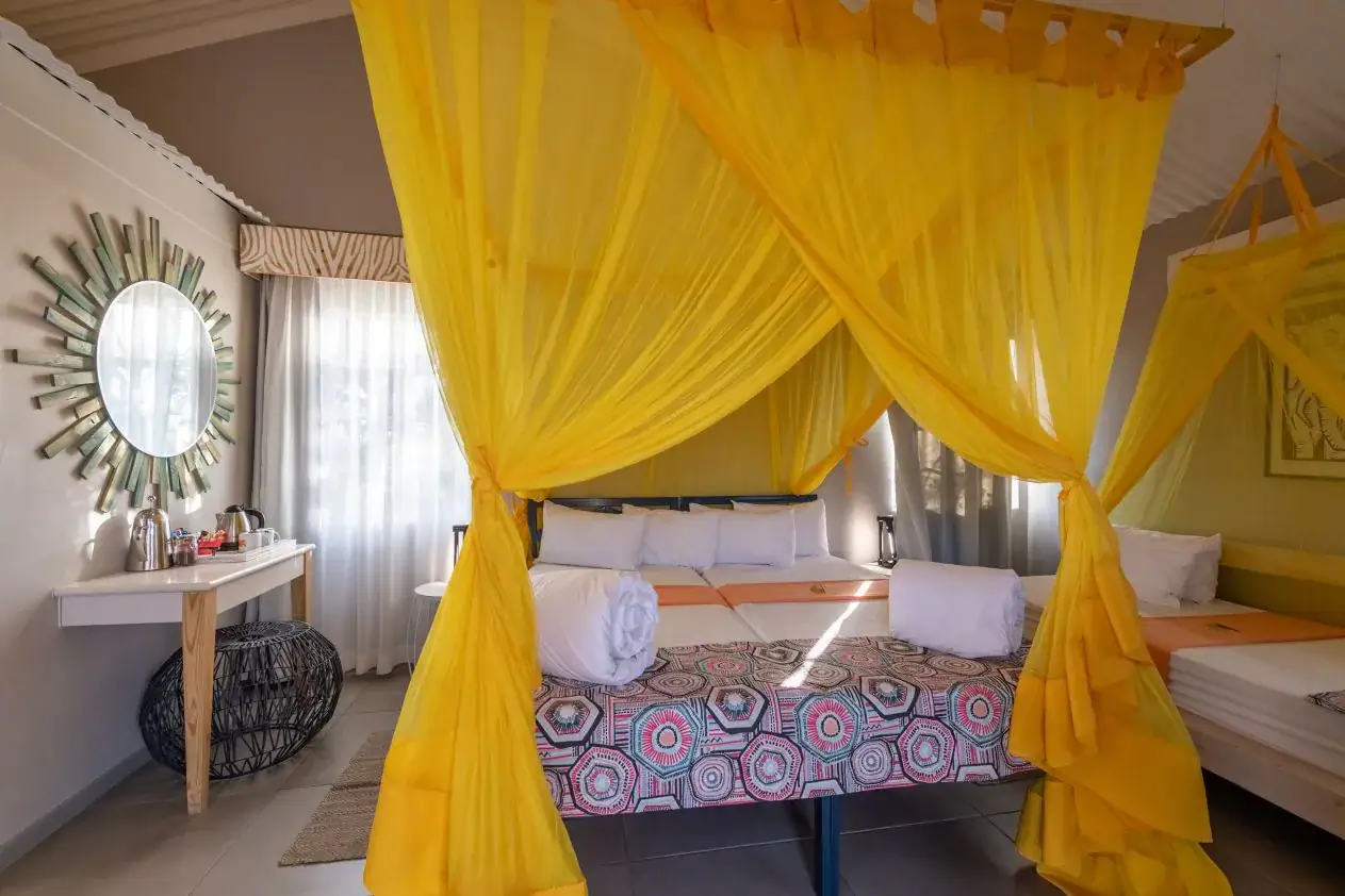 Twin beds under yellow mosquito-net canopies with patterned throws at Etosha Safari Camp