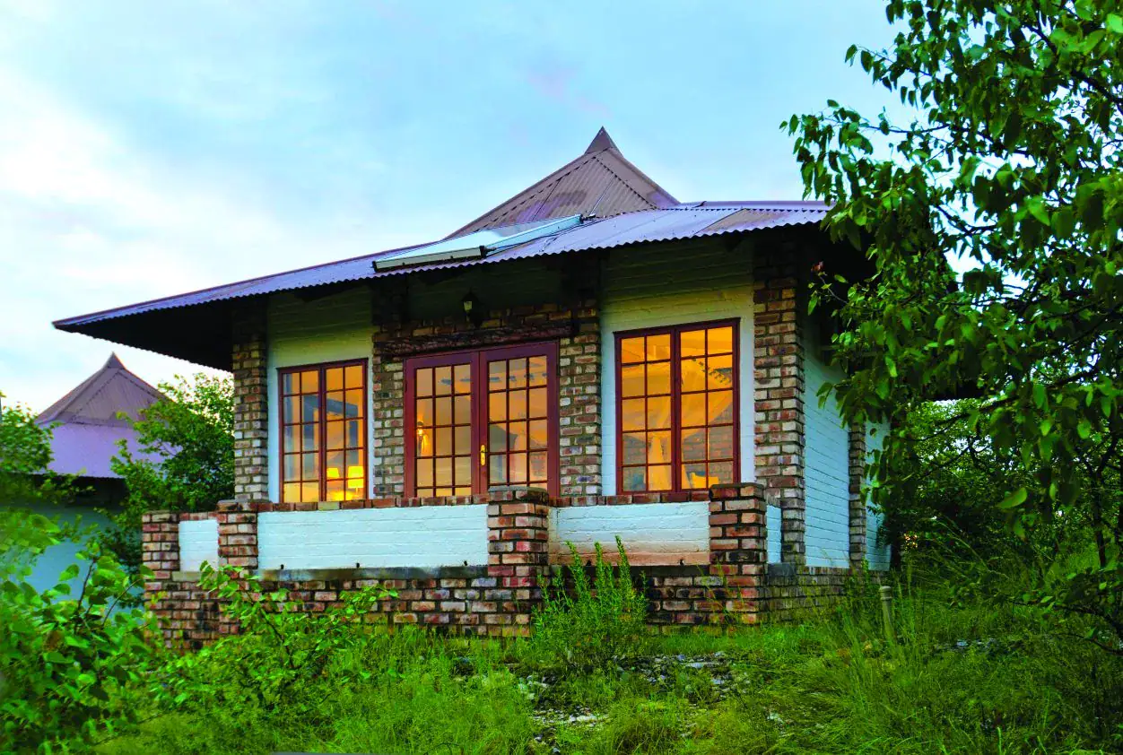 Brick-and-white guest bungalow glowing with warm window light at dusk at Etosha Safari Lodge