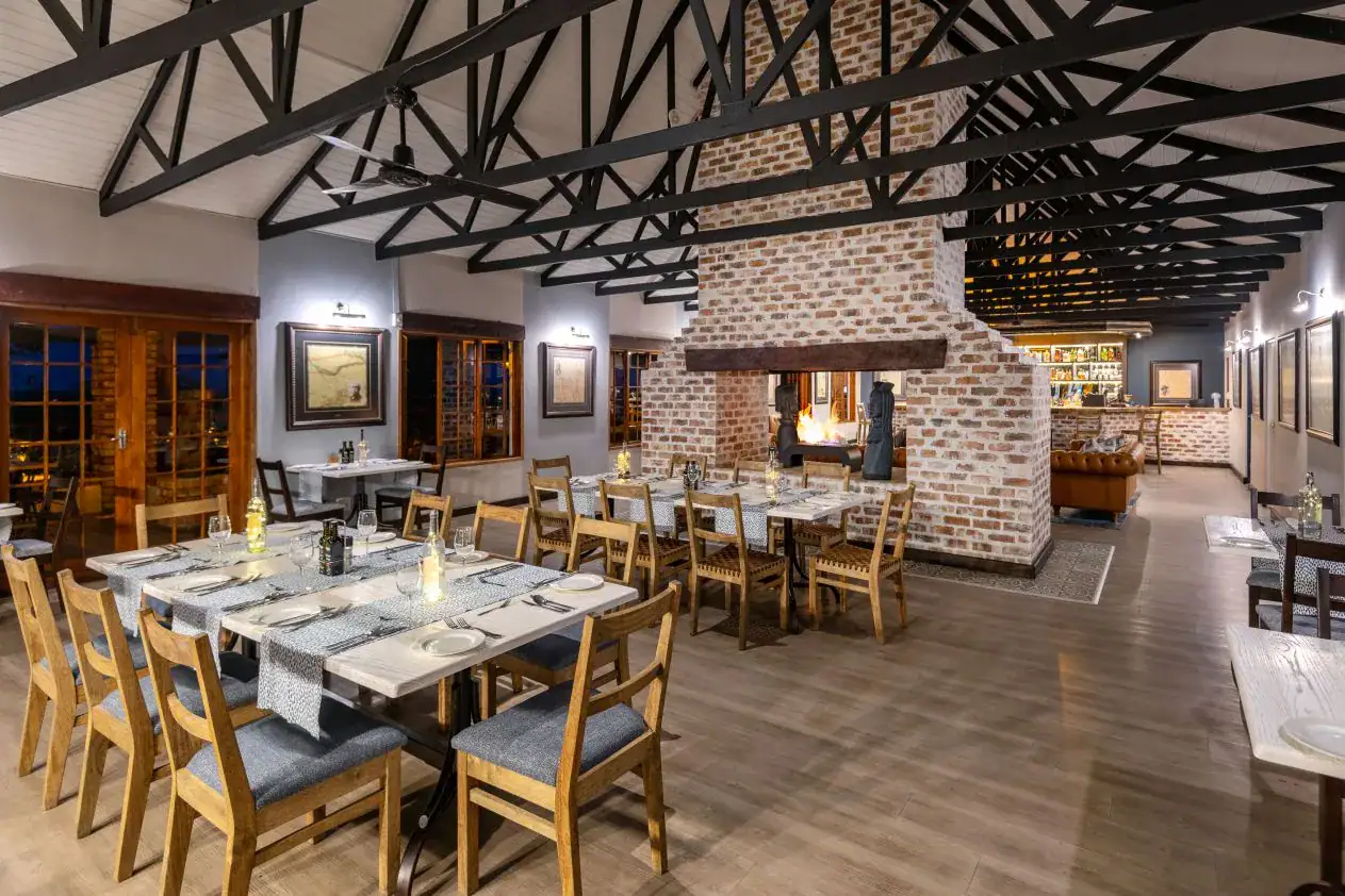 Restaurant with whitewashed-brick double fireplace and wooden tables at Etosha Safari Lodge