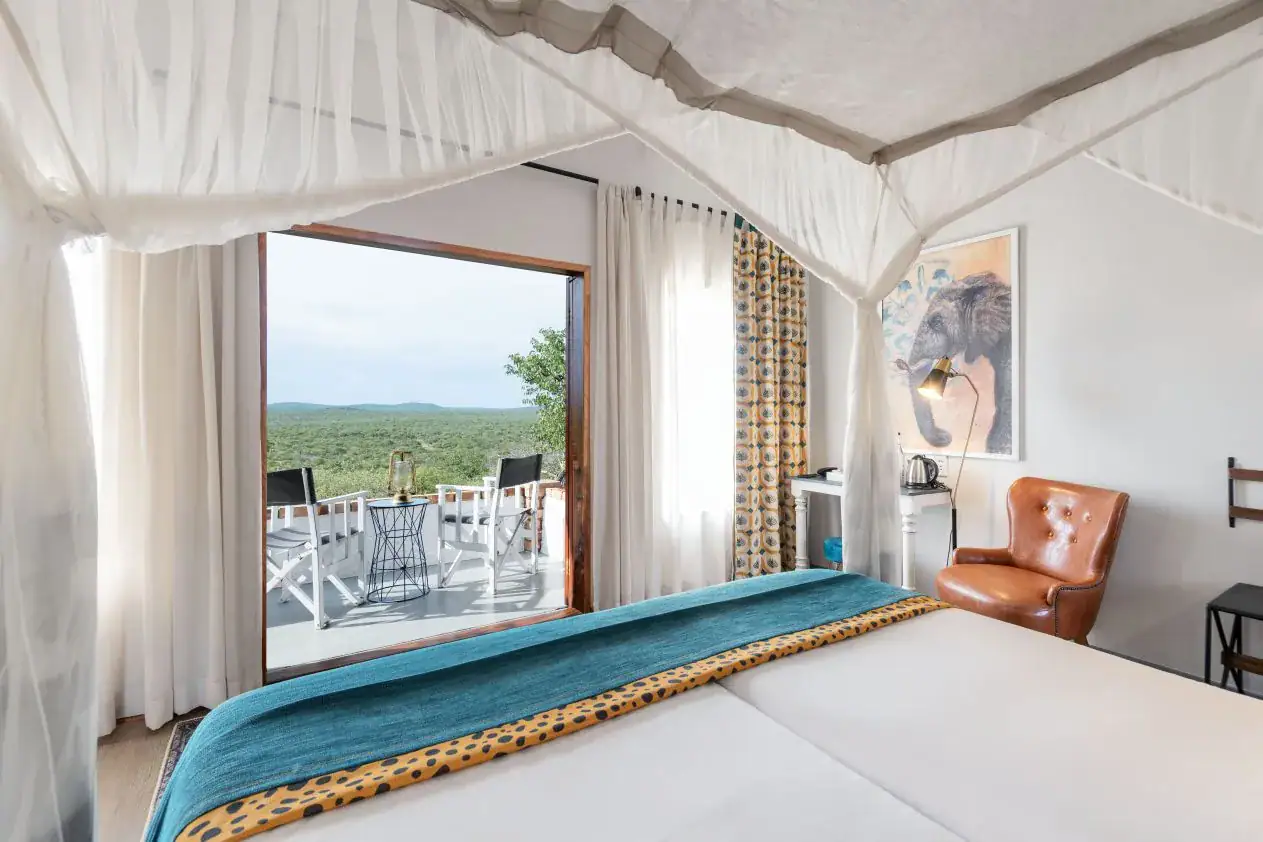 Four-poster canopy bed facing open balcony doors with a savannah view at Etosha Safari Lodge