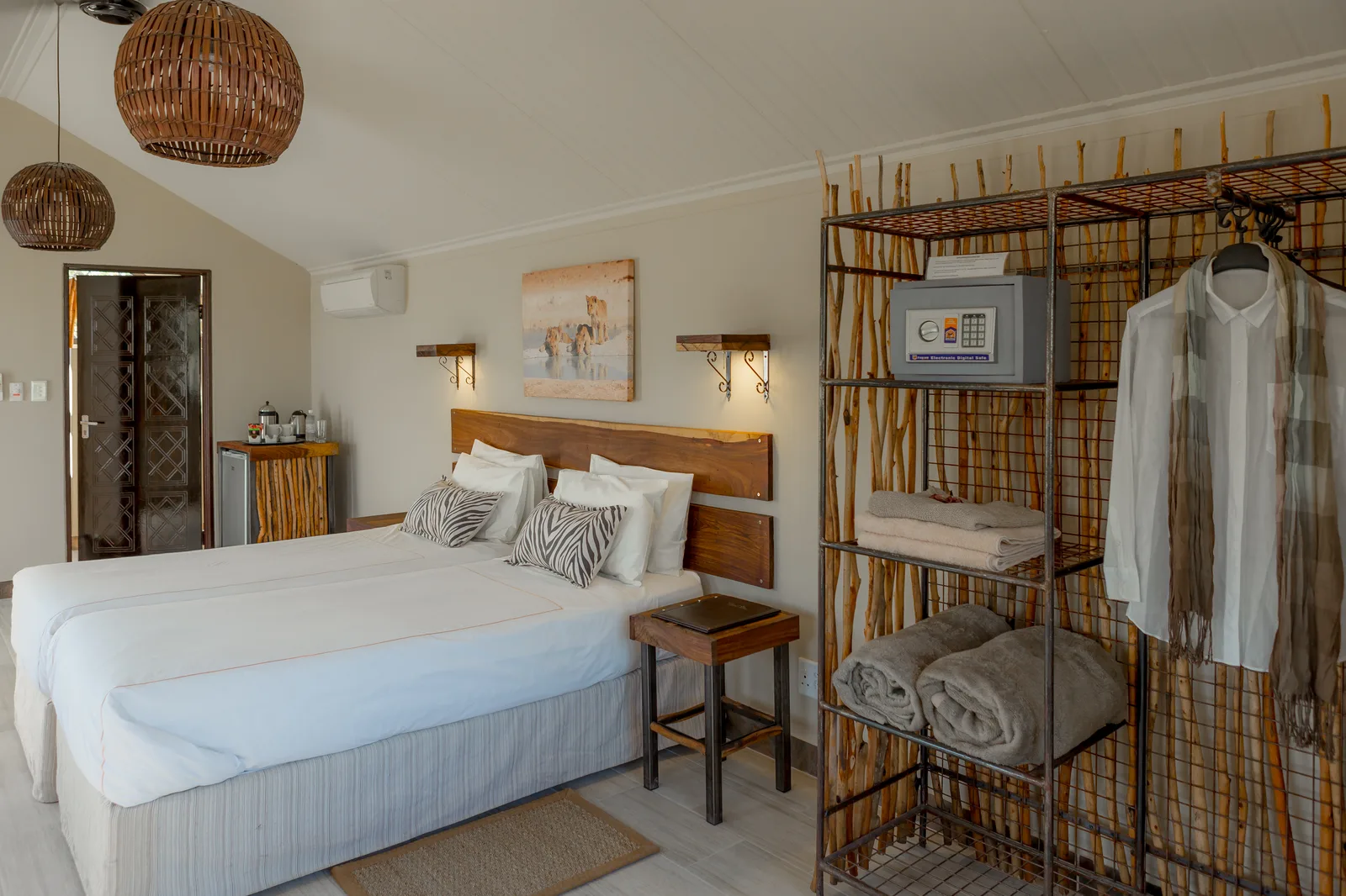 Tented unit interior at Etosha Village with double bed, wildlife art and rattan pendant lights in the evening