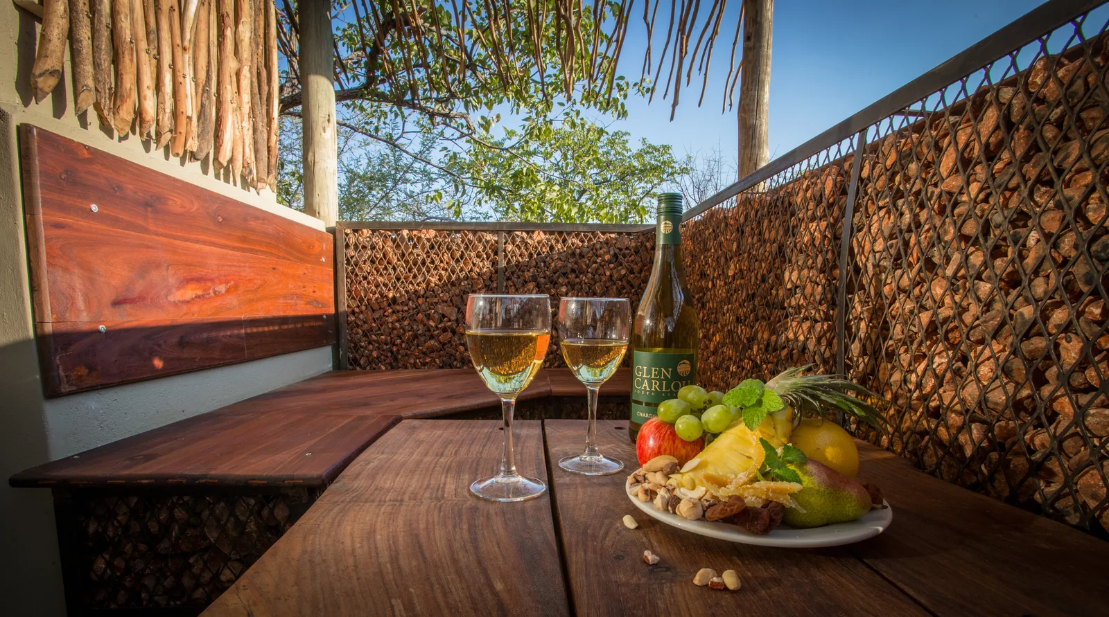 Private tented-unit patio at Etosha Village set with wine and a fruit platter on a timber table