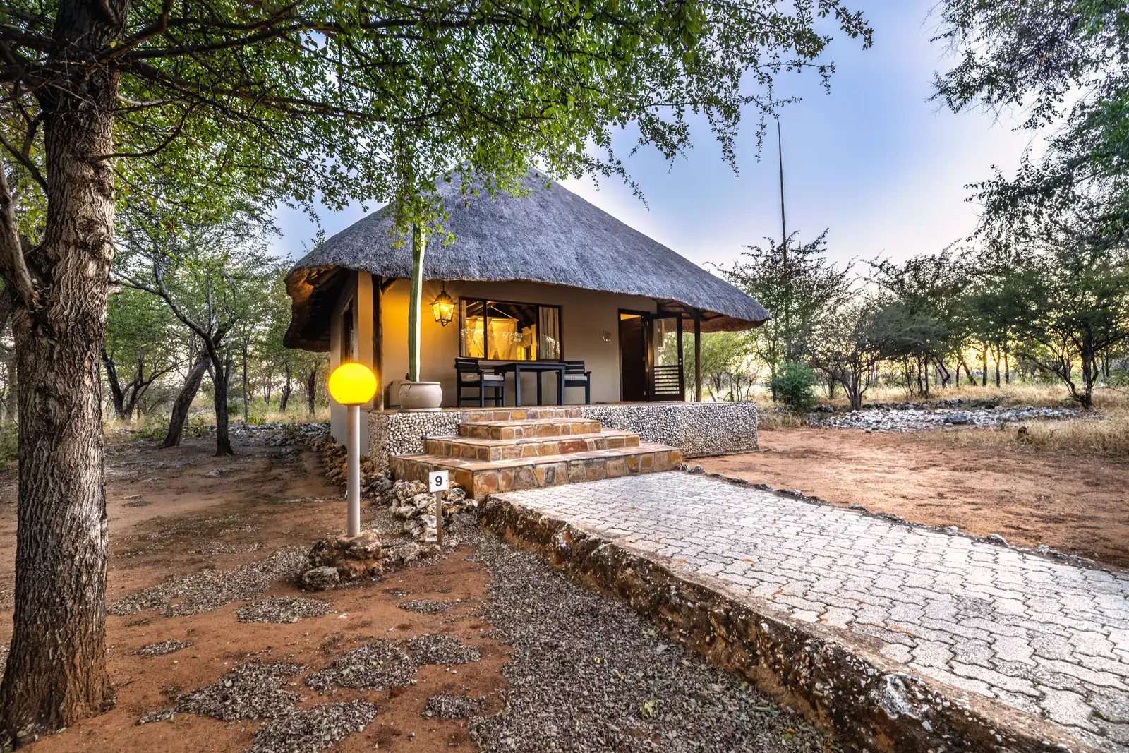 Thatched chalet at Mushara Lodge glowing at dusk with stone steps and paved walkway