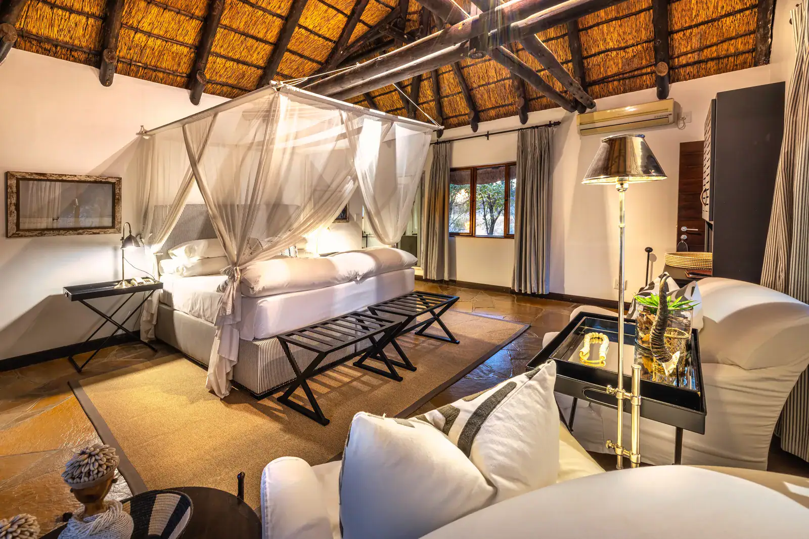 Chalet bedroom at Mushara Lodge with net-draped canopy bed and soaring thatch-and-timber ceiling