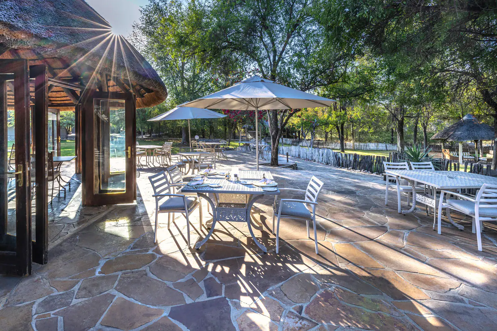Sunlit flagstone terrace with umbrella-shaded dining tables beside the gardens at Mushara Lodge