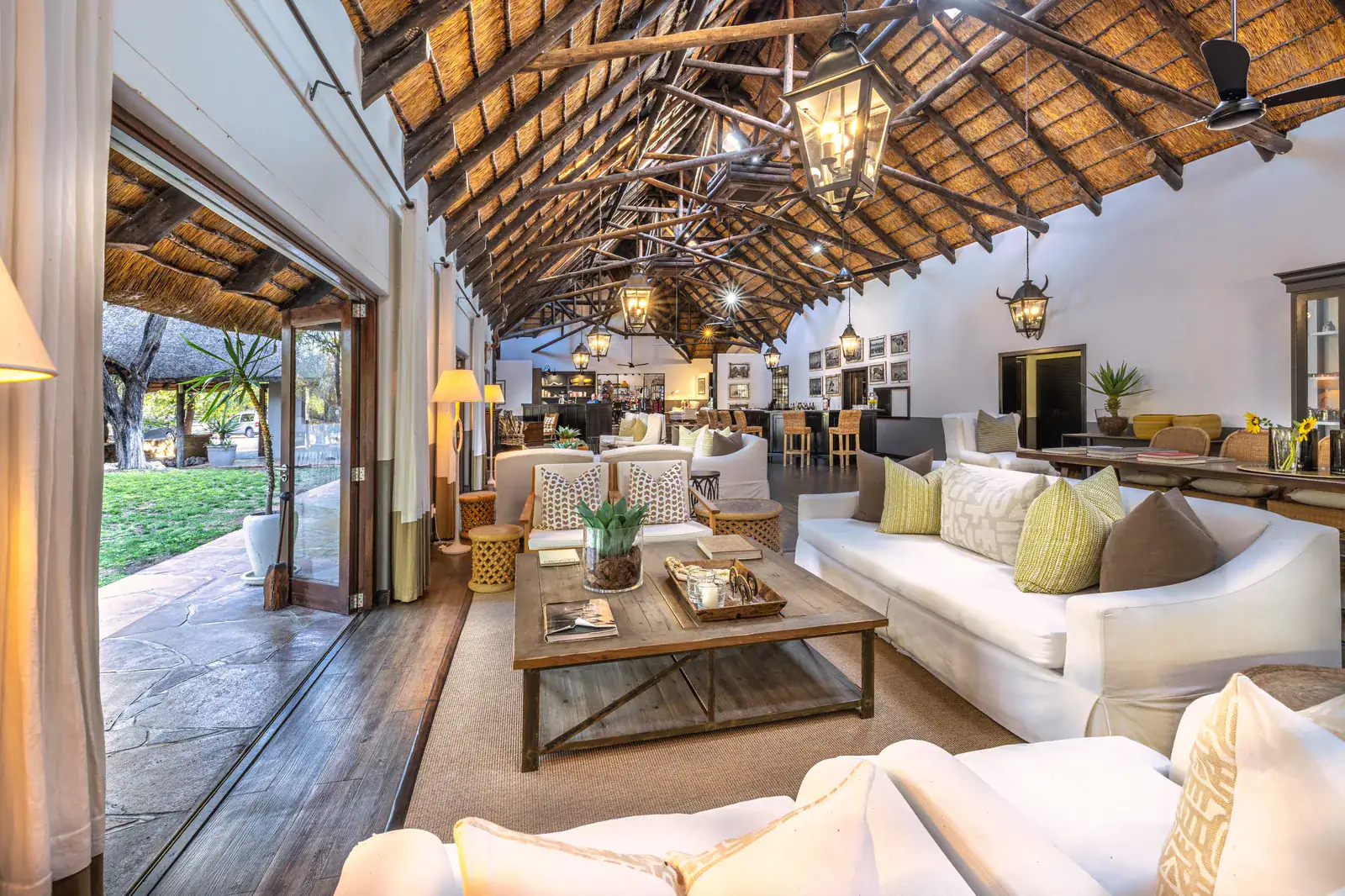 Open-sided thatched lounge at Mushara Lodge with white sofas and doors opening onto the garden