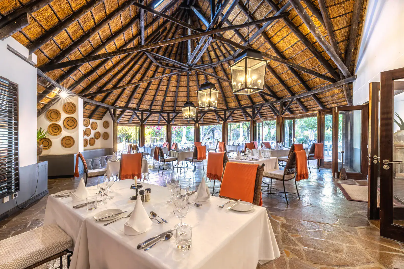 Restaurant at Mushara Lodge under a high thatched roof with white-clothed tables and lantern chandeliers
