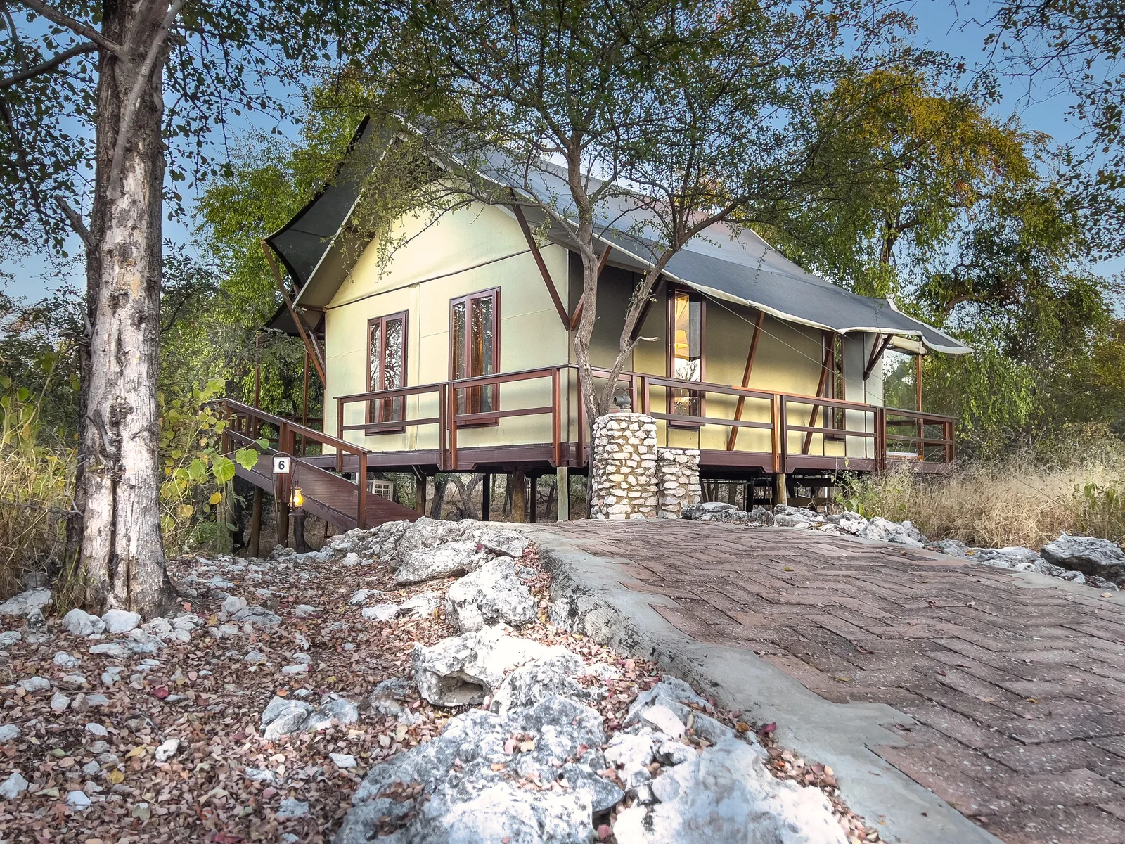 Luxury tented bungalow on a raised wooden deck glowing at dusk at Mushara Outpost