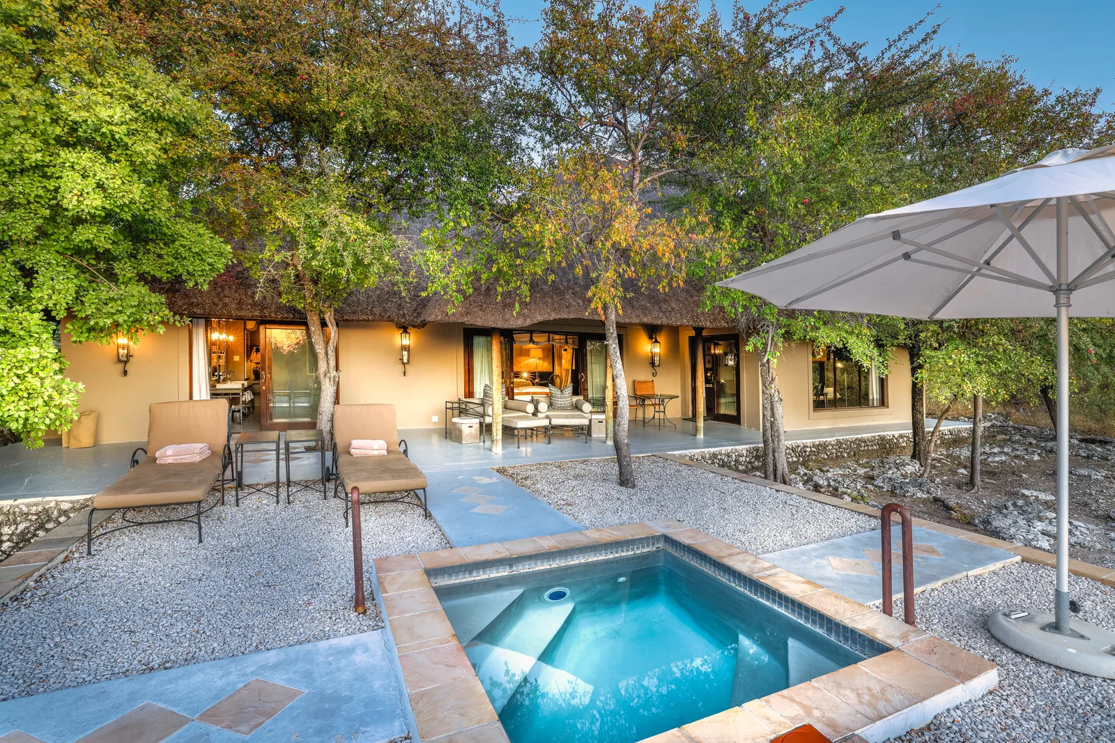 Private plunge pool and sun loungers in front of a thatched Villa Mushara villa at dusk
